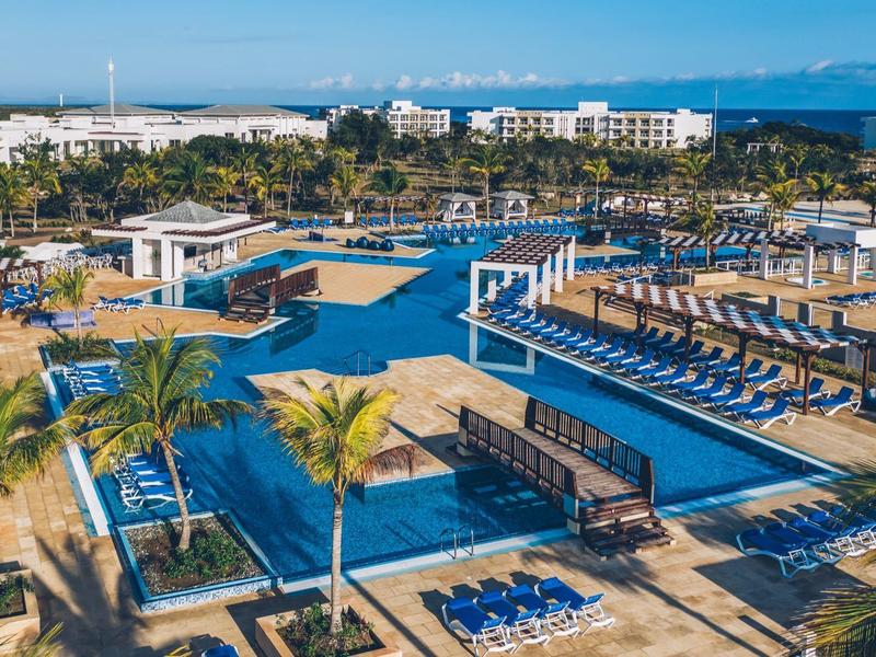 Velká hotelová oblast s několika bazény, lehátky a palmami pod čistou oblohou.