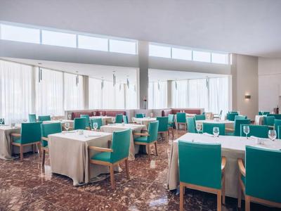 Helles, modernes Restaurant mit türkisfarbenen Stühlen und weißen Tischdecken, großen Fenstern.