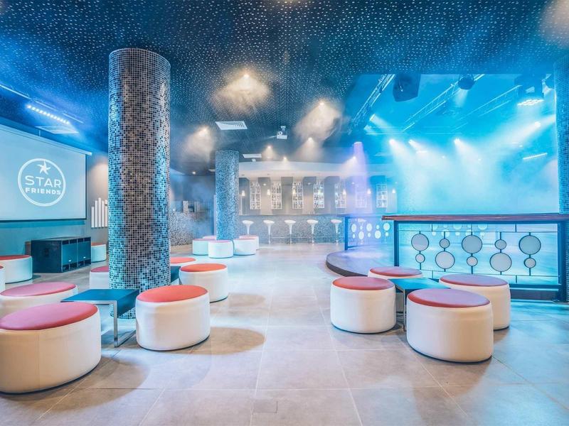 Moderner Clubraum mit runden weißen Hockern, rosafarbenen Sitzpolstern und blauer Atmosphäre.