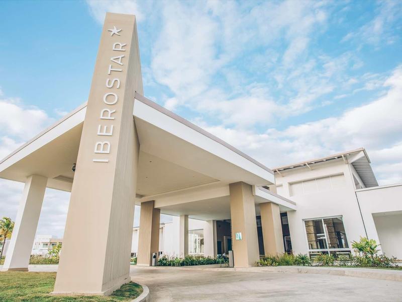 Modernes Gebäude mit großem Eingangsbereich und Säulen, hell gestrichen, unter blauem Himmel.