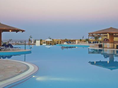 Gran piscina al aire libre con vista al mar y dos áreas cubiertas al atardecer.