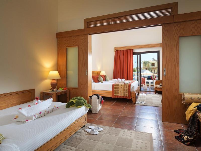 Habitación de hotel luminosa con dos áreas, cama individual, sofá, elementos de madera y vista al balcón.