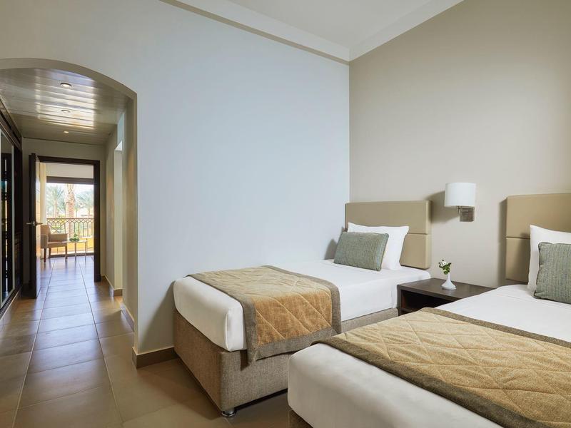 Nowoczesny pokój hotelowy z dwoma pojedynczymi łóżkami i beżowymi kołdrami.