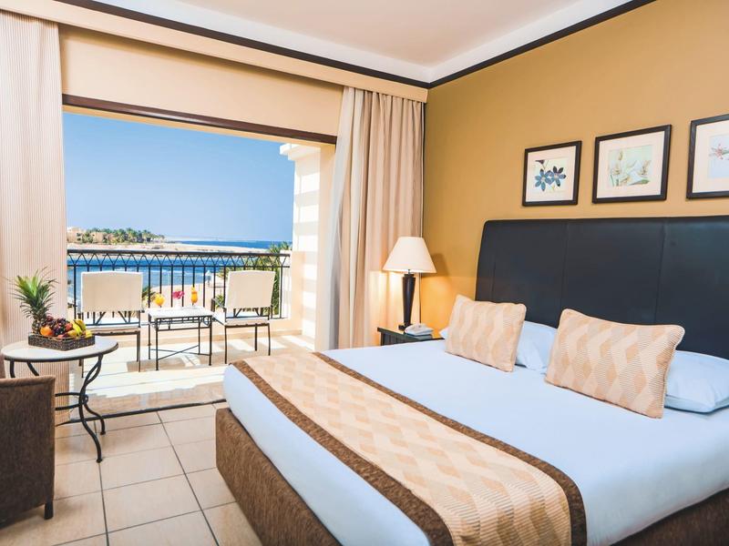 Elegancki pokój hotelowy z dużym łóżkiem i balkonem z widokiem na morze.