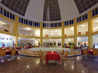 Duży hol hotelowy z czerwonymi stołami i centralną fontanną pod przeszklonym dachem.