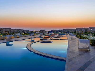 Rozległy basen z zachodem słońca i leżakami w ośrodku.