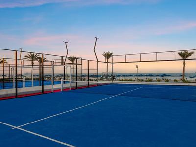 Blauer Paddle-Tennisplatz mit Stahlnetz und Abendhimmel im Hintergrund