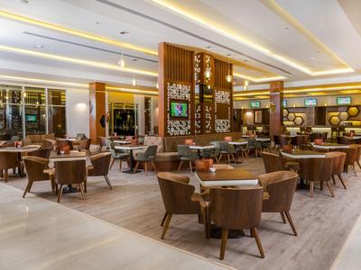 Nowoczesna restauracja z eleganckimi drewnianymi meblami i ciepłym oświetleniem w hotelowym wnętrzu.