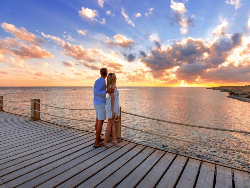 Un couple debout sur une jetée en bois au coucher du soleil au bord de la mer.