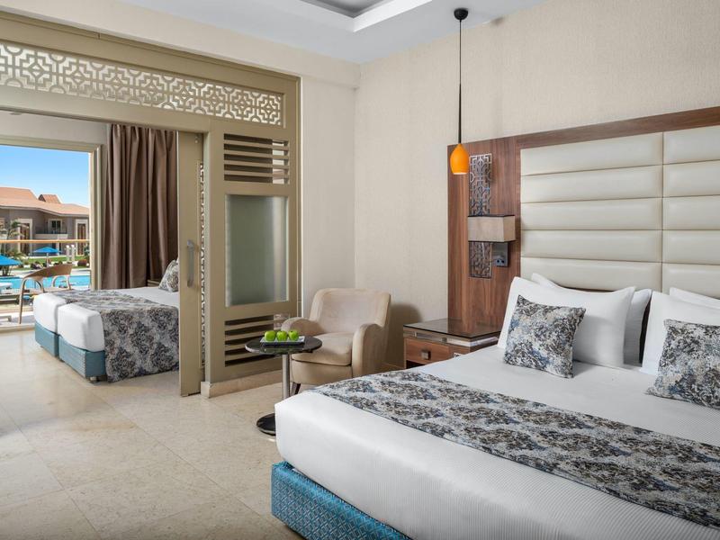 Chambre d'hôtel moderne avec grand lit, fauteuil, balcon et vue sur piscine.