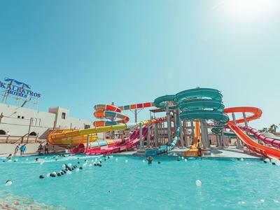 Area con scivoli d'acqua colorati e piscina piena di bagnanti con sole splendente.