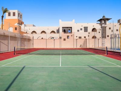 Campo da tennis con superficie rossa e verde davanti a un edificio chiaro sotto un cielo azzurro.