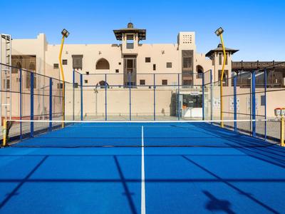 Campo da paddle tennis blu davanti a un edificio tradizionale chiaro sotto un cielo sereno.