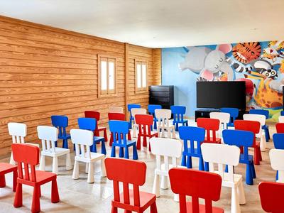 Bunter Kindersaal mit kleinen roten, weißen und blauen Stühlen vor einer Wand mit Tiermotiv.