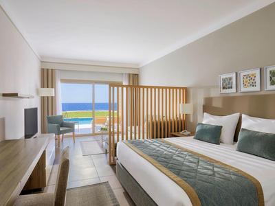 Modernes Hotelzimmer mit Doppelbett, Holzwand, Balkon und Meerblick bei Tageslicht.