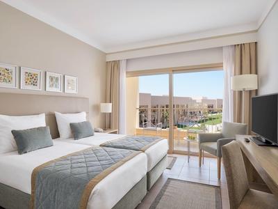 Helles Hotelzimmer mit Doppelbett, modernem Mobiliar und großem Fenster mit Balkon und Aussicht.