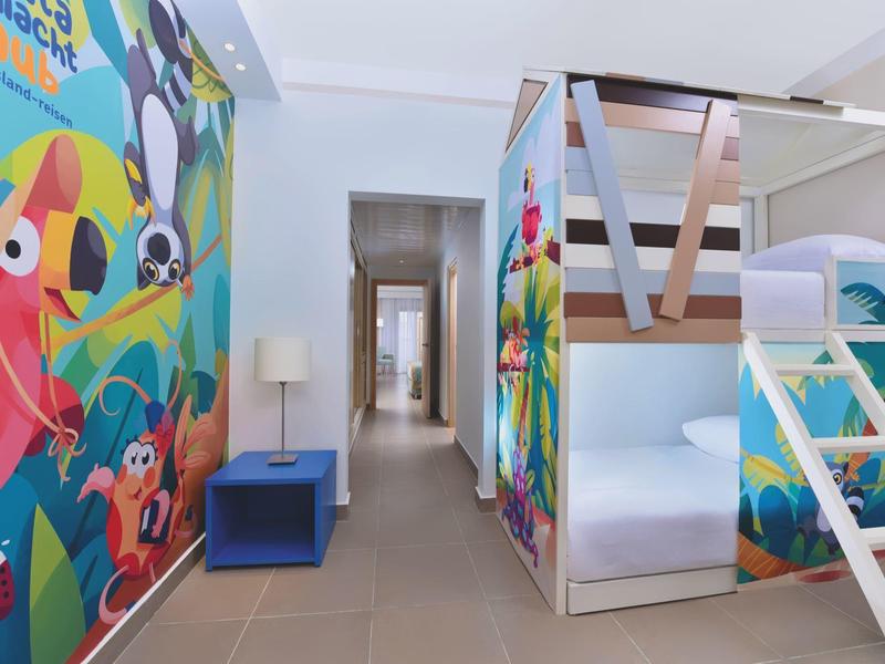 Kinderzimmer mit Etagenbett, bunten Wandbildern, blauem Nachttisch und hellem Fliesenboden.