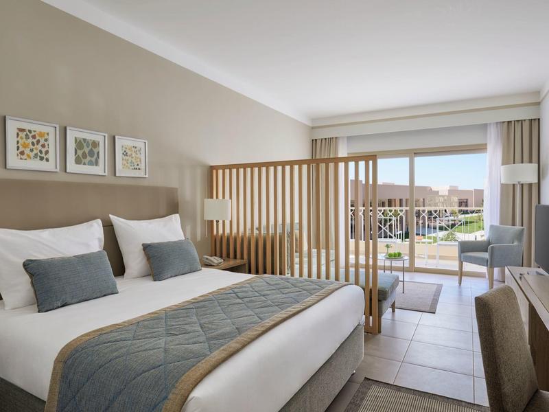 Modernes Hotelzimmer mit Doppelbett, Holzgittertrennwand und Blick auf Balkon und Außenbereich.