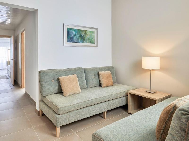 Hell eingerichtetes Wohnzimmer mit grünem Sofa, zwei Kissen, Holztisch und stehendem Lampenschirm.