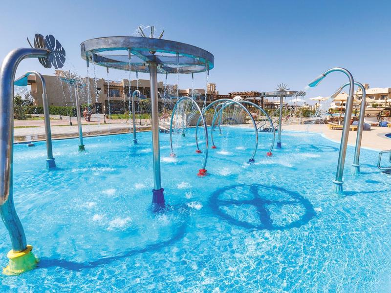 Buitenspeelbad met verschillende sproeifuncties in een hotelzwembad onder een heldere hemel.