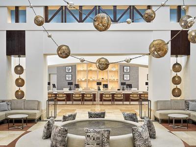Moderner heller Raum mit großen Kronleuchtern, Sofas, Kissen und Bar im Hintergrund.
