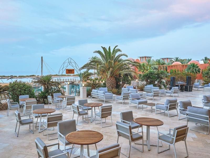 Leere Außenlounge mit modernen Sesseln und Tischen, Palmen und Meer im Hintergrund am Abend.