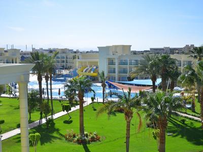 Hotel mit Pool, Palmen und gepflegtem grünen Rasen unter blauem Himmel.