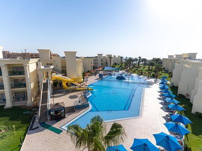 Großer Hotelpool mit blauen Sonnenschirmen und angelegten Gebäuden bei klarem Himmel.