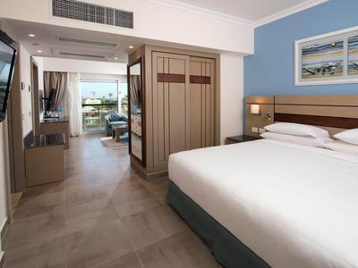 Modernes Hotelzimmer mit großem Bett, Fernseher und Blick auf einen Balkon.