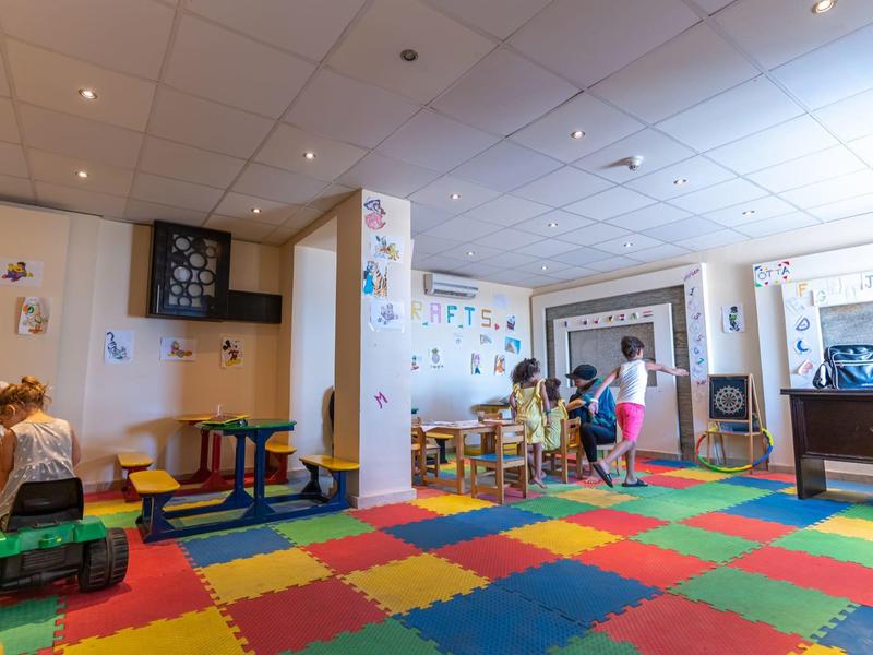 Großer bunter Spielraum mit weichem Schaumstoffboden, Tischen, Stühlen und Kindern, die spielen.