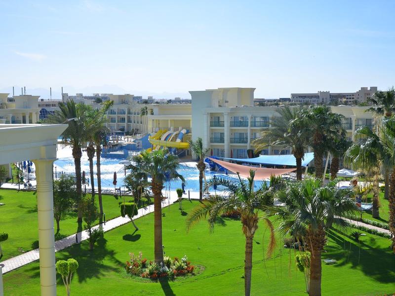 Hotel mit Pool, Palmen und gepflegtem grünen Rasen unter blauem Himmel.