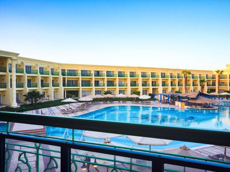 Großes Hotel mit mehreren Stockwerken, großem Pool und vielen Liegestühlen unter blauem Himmel.