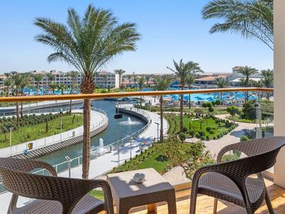 Balkon mit zwei Stühlen und Tisch blickt auf Wasserkanal, Palmen und weitläufige Hotelanlage bei Sonnenschein.