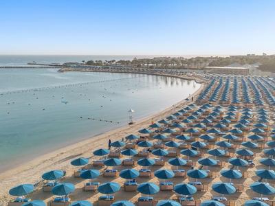 Strand mit Reihen von blauen Sonnenschirmen und ruhigem Meer unter klarem Himmel bei Sonnenaufgang.