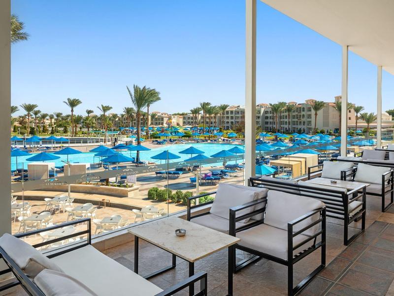 Großzügige Hotelterrasse mit Sitzgelegenheiten und Blick auf Poolbereich mit blauen Sonnenschirmen.