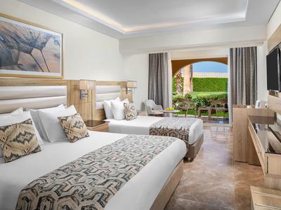 Geräumiges Hotelzimmer mit zwei Betten, Holzmöbeln, großem Fenster und Blick auf Terrasse und Garten.
