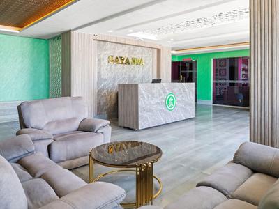 Einladender Hotel-Empfang mit grauen Sofas, Rundtisch und heller Marmortheke vor grünem Hintergrund.