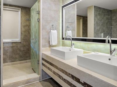 Modernes Badezimmer mit zwei weißen Waschbecken, großem Spiegel und ebenerdiger Dusche mit Glaswand.