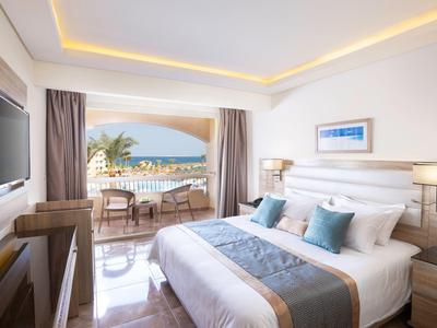 Helles Hotelzimmer mit Doppelbett, Balkon, Meerblick und moderner Einrichtung.