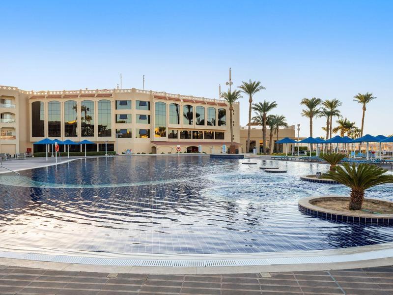 Moderner Hotelkomplex mit großem Pool und Palmen in sonniger Lage.