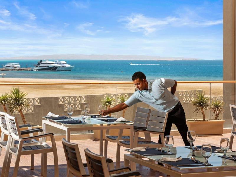 Mann deckt Terrasse mit Meerblick im Hintergrund für Gäste ein.