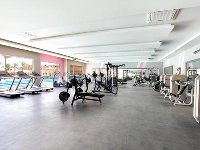 Großer, heller Fitnessraum mit verschiedenen Trainingsgeräten und großen Fenstern.