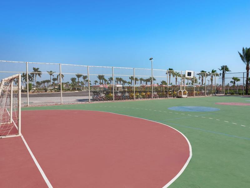 Leerer Outdoor-Sportplatz mit Fußballtor und Palmen im Hintergrund bei klarem Himmel.