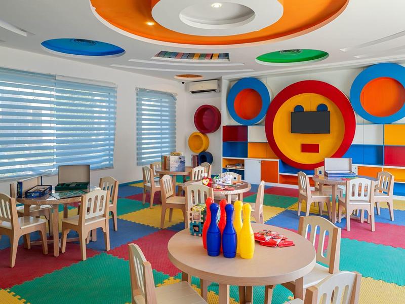 Bunter Kindergartenraum mit Stühlen, Tischen, Spielfiguren und runder Wandgestaltung.