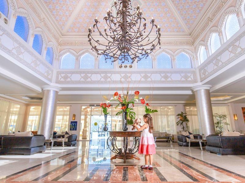 Große helle Hotellobby mit Kronleuchter, Marmorboden und Mittelarrangement aus Blumen.