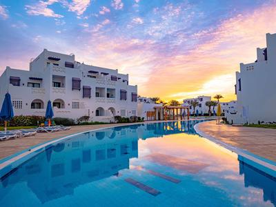 Moderner Hotelpool bei Sonnenuntergang mit weißen Gebäuden und blauem Himmel.