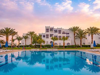 Ein Hotel mit Swimmingpool und Palmen bei Sonnenuntergang.