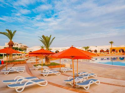 Leere Liegestühle und orangefarbene Sonnenschirme neben einem Pool unter blau bewölktem Himmel.