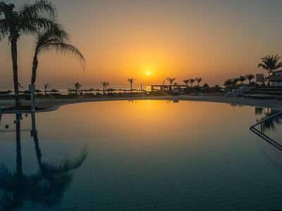 Ein Pool spiegelt den Sonnenuntergang mit Palmen und einer entspannten Atmosphäre wider.