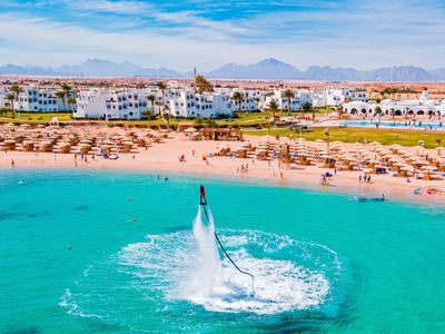 Person auf Flyboard über klarem blauem Wasser nahe Strand mit Strandliegen und Hotelgebäuden